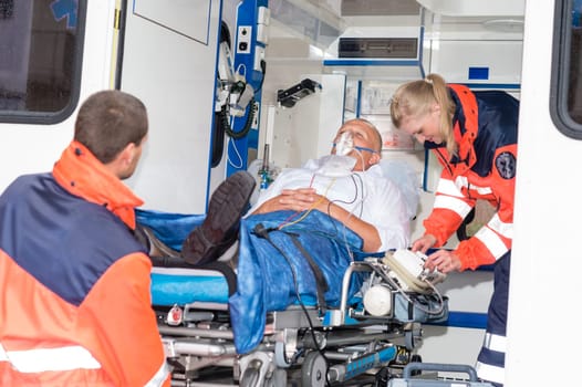 Paramedics putting patient man oxygen mask in ambulance car