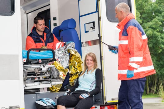 Woman in ambulance with emergency paramedics aid bike accident smiling
