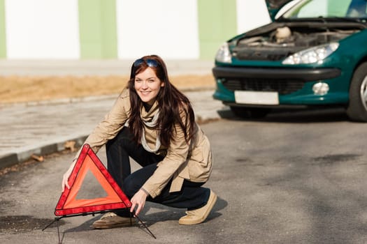 Woman putting warning triangle on the road car breakdown sign