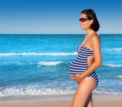 Beautiful pregnant woman walking on blue beach in summer vacation