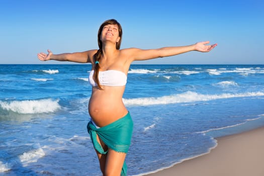 Beautiful pregnant woman walking on blue beach in summer vacation with open arms