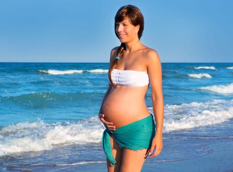 Beautiful pregnant woman walking on blue beach in summer vacation