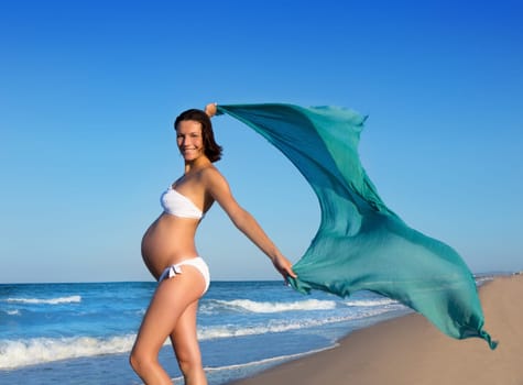 Beautiful pregnant woman walking on blue beach in summer with blowing wind handkerchief