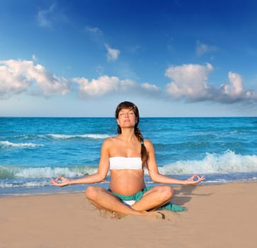Beautiful pregnant woman practicing yoga in blue beach sand on summer vacation