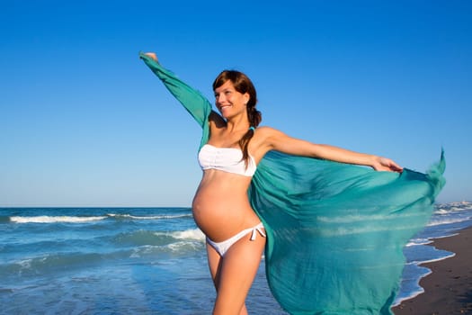 Beautiful pregnant woman walking on blue beach in summer with blowing wind handkerchief