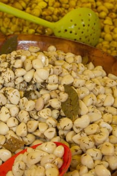 Pickled garlic with spices and herbs at the market. Olives in the background.