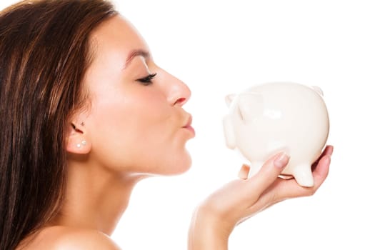 Beautiful young woman kissing piggy bank against white background