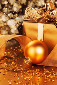 Golden Christmas bauble next to Christmas gift in golden light