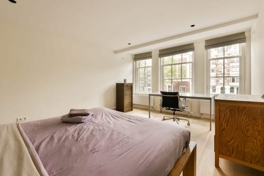 a bedroom with a bed, desk and window overlooking the cityscapet is on the right side of the room