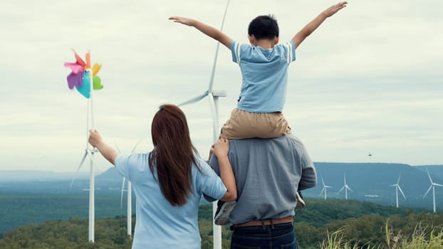 Concept of progressive happy family enjoying their time at the wind turbine farm. Electric generator from wind by wind turbine generator on the country side with hill and mountain on the horizon.