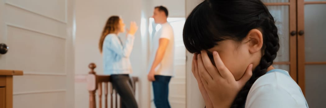 Stressed and unhappy young girl huddle in corner, cover her face while her parent arguing in background. Domestic violence at home and traumatic childhood develop to depression. Panorama Synchronos