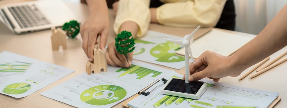 Windmill model represented using renewable energy placed during presenting green business on table with wooden block and environmental document scatter around. Closeup. Delineation.