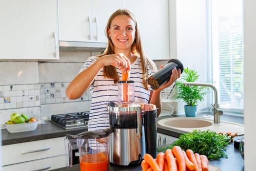 A woman making carrot juice from fresh carrots with a home juicer in the kitchen. Healthy lifestyle