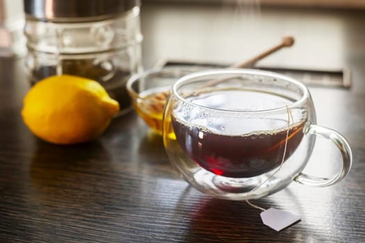 Cup of hot black tea, bowl with honey and lemon on a wooden table.