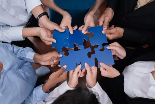 Diverse corporate officer workers collaborate in office, connecting puzzle pieces to represent partnership and teamwork. Unity and synergy in business concept by merging jigsaw puzzle. Concord