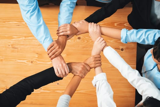 Multicultural business people holding hand together in circle. Unity teamwork in office business workplace. Diverse ethnic office worker engaged in team building. Habiliment