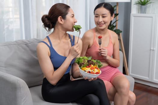 Young sporty Asian women in sportswear holding salad bowl together fill with vibrant of fruit and vegetable. Natural youthful and fit body lifestyle with balance nutrition and home exercise. Vigorous