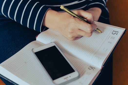 woman freelancing online. A businesswoman working in her home office and making notes in her diary. woman makes notes in a notebook while working with a smartphone