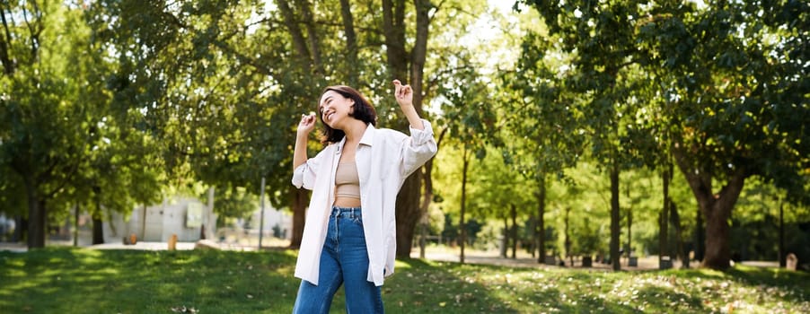 Portrait of happy girl dancing and looking happy, posing in park, enjoying herself, walking alone, feeling freedom and excitement.