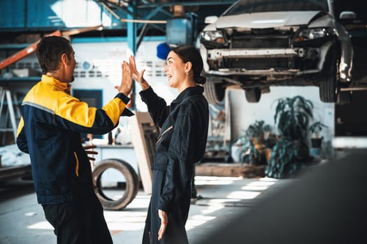 Two happy vehicle mechanic celebrate and high five after made successful car inspection or repair in automotive service car workshop. Technician team enjoy accomplishment together in garage. Oxus