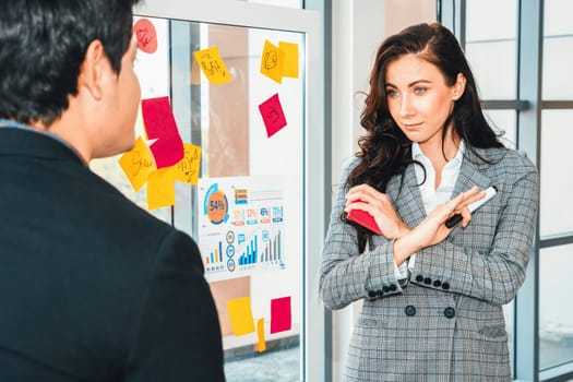 Business people work on project planning board in office and having conversation with coworker friend to analyze project development . They use sticky notes posted on glass to make it organized. Jivy