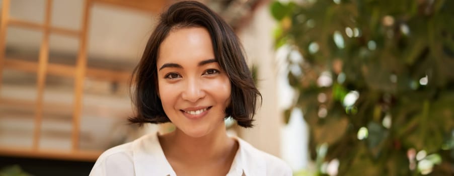 Close up portrait of beautiful brunette asian girl, smiling and looking flirty at camera, chuckle cute. Copy space