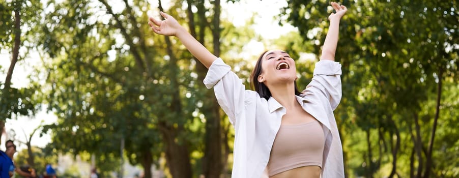 Portrait of carefree young asian woman dancing in park alone, enjoying freedom, smiling with joy. Copy space