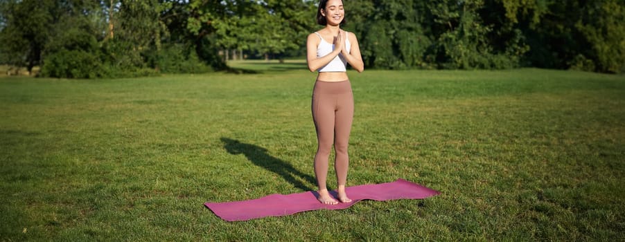 Mindfulness and wellbeing. Young woman doing yoga, standing on mat in park, making asana, meditating on fresh air, urban life concept.