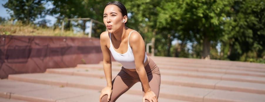 Portrait of sportswoman panting, taking break during jogging training, sweating while running outdoors.