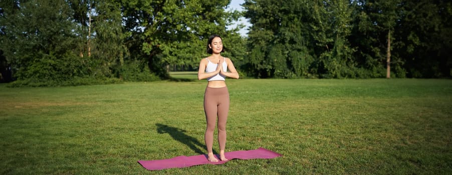 Mindfulness and wellbeing. Young woman doing yoga, standing on mat in park, making asana, meditating on fresh air, urban life concept.