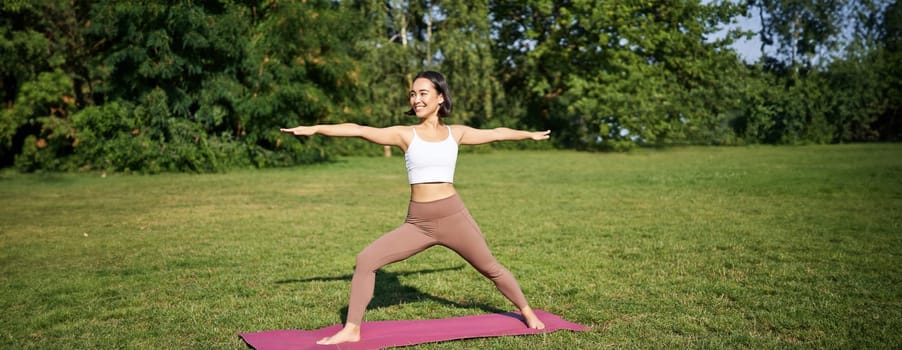 Young woman stretching her body, workout and doing yoga in park, standing on rubber mat in fitness clothing during training session.