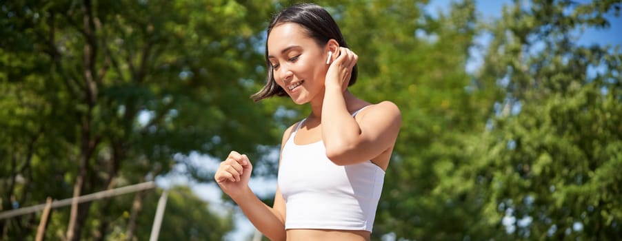 Wellbeing. Smiling asian fitness girl, runner in park, smiling and running, doing jogging workout outdoors on streets.