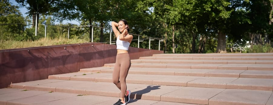 Portrait of young sportswoman running on street. Fitness girl jogging in park, workout outdoors, listening music in wireless earphones.