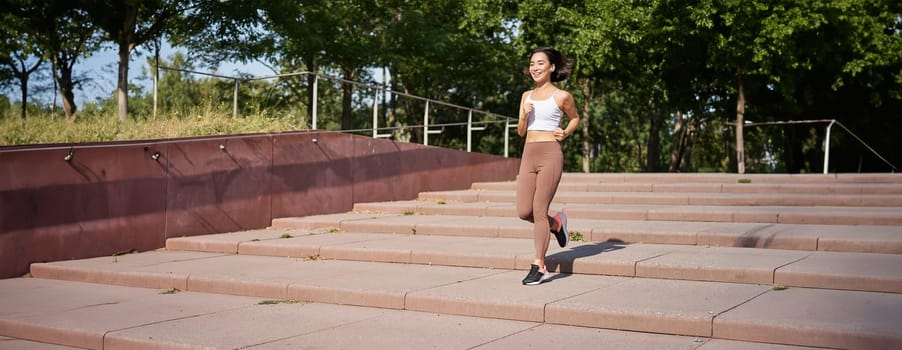 Healthy fitness girl running outdoors on street, wearing uniform, jogging on fresh air and listening music in wireless headphones.