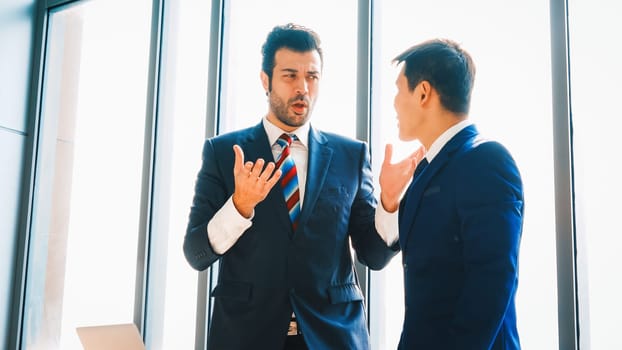 Two business people talk project strategy at office meeting room. Businessman discuss project planning with colleague at modern workplace while having conversation and advice on financial report. Jivy