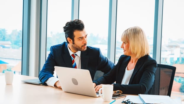 Two business people talk project strategy at office meeting room. Businessman discuss project planning with colleague at modern workplace while having conversation and advice on financial report. Jivy