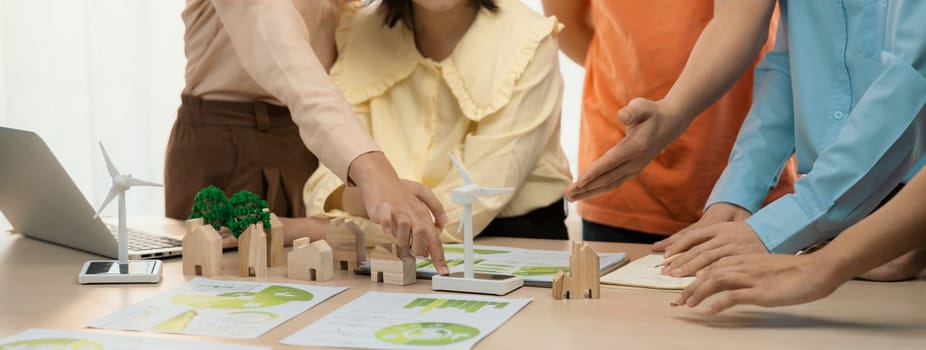 Windmill model represented using renewable energy placed during presenting green business on table with wooden block and environmental document scatter around. Closeup. Delineation.