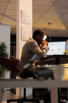 Businessman stting at desk in front of computer drinking coffee before start planning company strategy, working late at night at investment plan in startup office. Business concept
