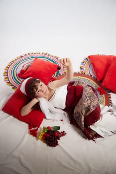 Portrait of Little girl in a stylized Tatar national costume with berries and a brush of grapes on a white background in the studio. Photo shoot of funny young teenager who is not a professional model