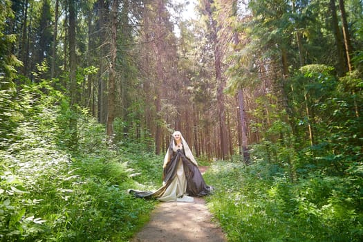 Adult mature woman 40-60 in a green long fairy dress in forest. Photo shoot in style of dryad and queen of nature. Fairy in beautiful green summer forest. Concept of caring for nature