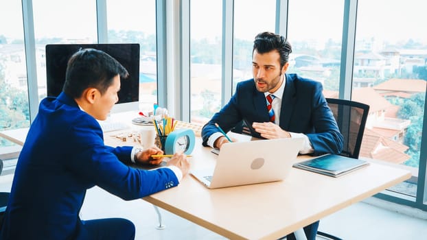 Two business people talk project strategy at office meeting room. Businessman discuss project planning with colleague at modern workplace while having conversation and advice on financial report. Jivy