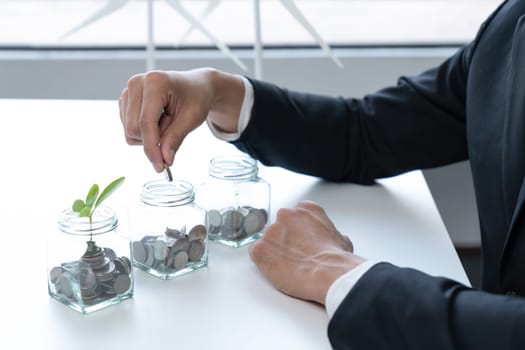 Businessman put coin to money saving glass jar at his office as sustainable money growth investment or eco-subsidize. Green corporate promot and invest in environmental awareness. Gyre