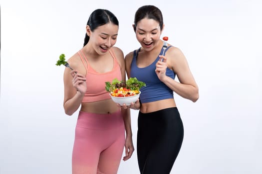 Two young sporty Asian women in sportswear holding salad bowl fill with fruit and vegetable. Natural youthful and fit body lifestyle people with balance nutrition on isolated background. Vigorous