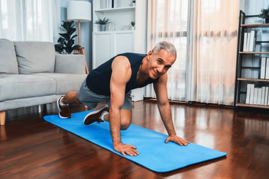 Athletic and active senior man doing exercise on fit mat with plank climbing at home exercise as concept of healthy fit body lifestyle after retirement. Clout