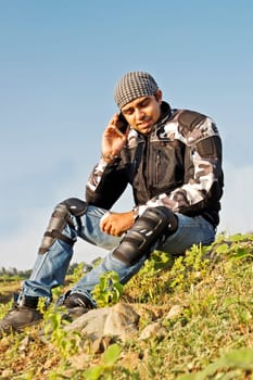 Young adult male in bikers gear sat at the roadside using a moblie phone. Generic shot, location India