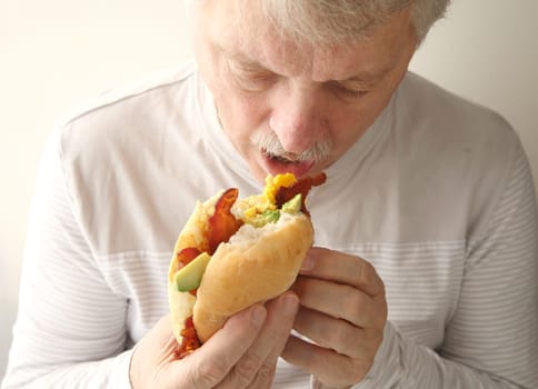 older man eats bacon, egg and avocado sandwich