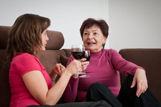 Smiling senior mother with daughter talking and drinking wine on sofa at home