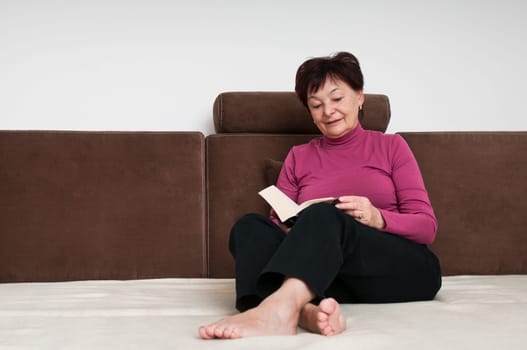 Mature woman reading book at home sitting on couch