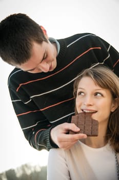 Young happy couple together outdoor - man gives chcolate to woman