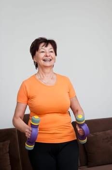 Smiling happy senior fitness woman excercising with barbells at home